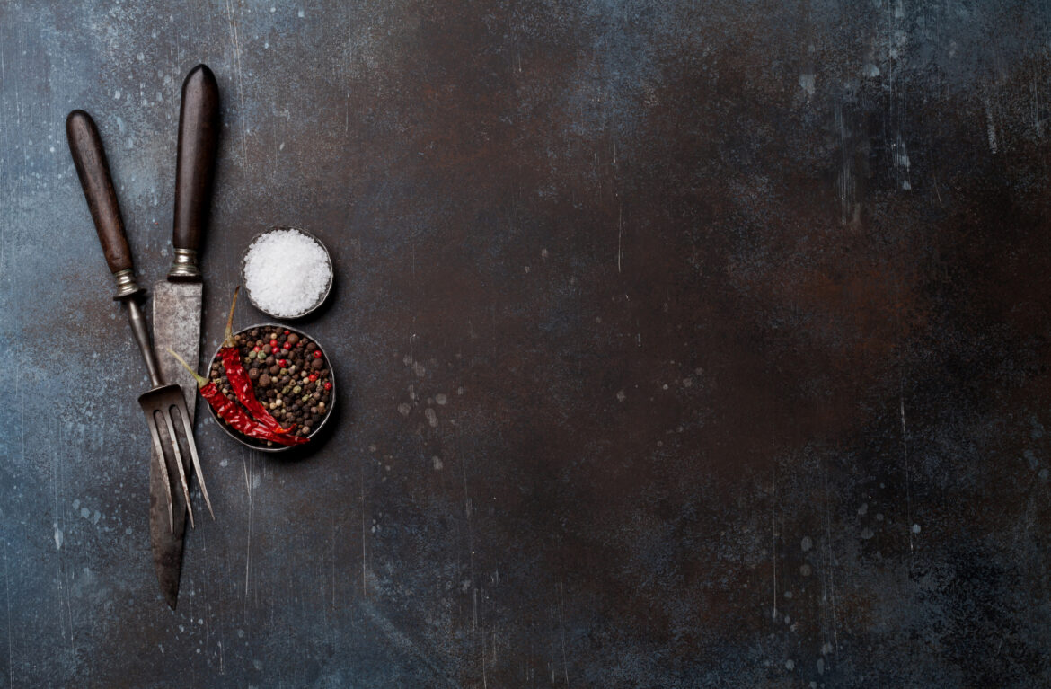 Vintage meat knife, fork and spices over stone table.